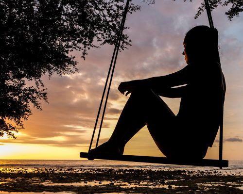 woman sits on swing, watches sunset